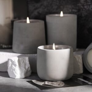 Three cement cups (different sizes) with burning candles on a wooden table, creating an industrial modern ambiance.