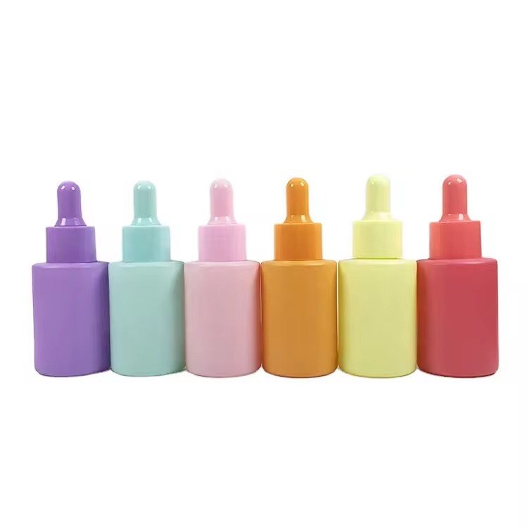 Assorted 30ml solid color essential oil bottles with droppers – purple, green, blue, pink, orange, yellow, red arranged on a table, top-down view