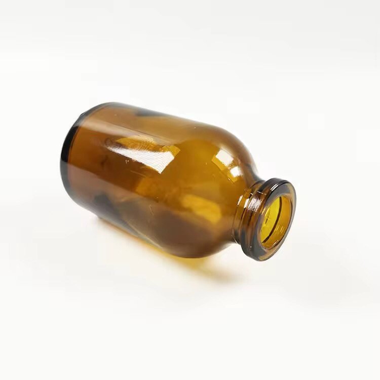 Empty amber aromatherapy bottle lying on its side on a wooden table – showing bottle shape, neck opening, and glass transparency